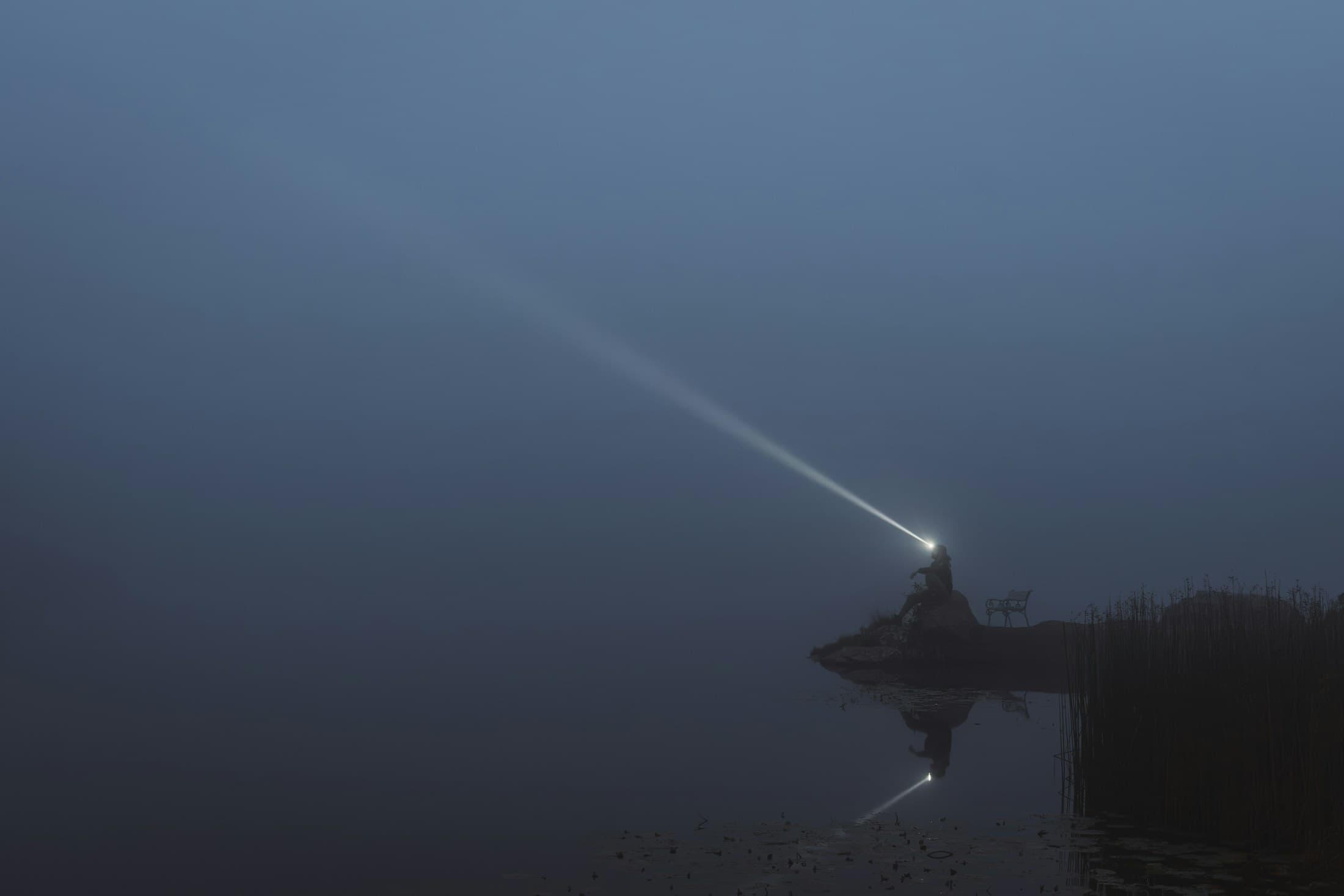 Snop światła przecinający ciemną, mglistą wodę nocą